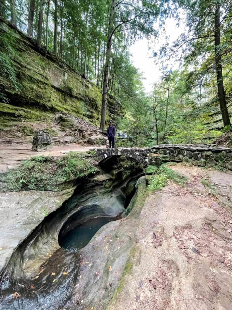 Man smiling while standing on bridge over the Devil's Bathtub in Hocking Hills