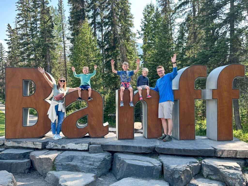 Mom, Dad, and 3 boys smiling by BANFF sign in Banff, Canada