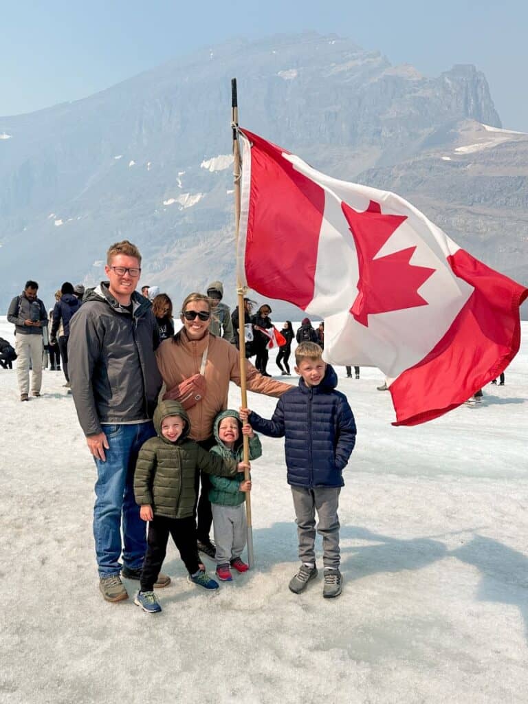 Family standing on glacier with Canadian flag during Columbia Icefields Adventure
