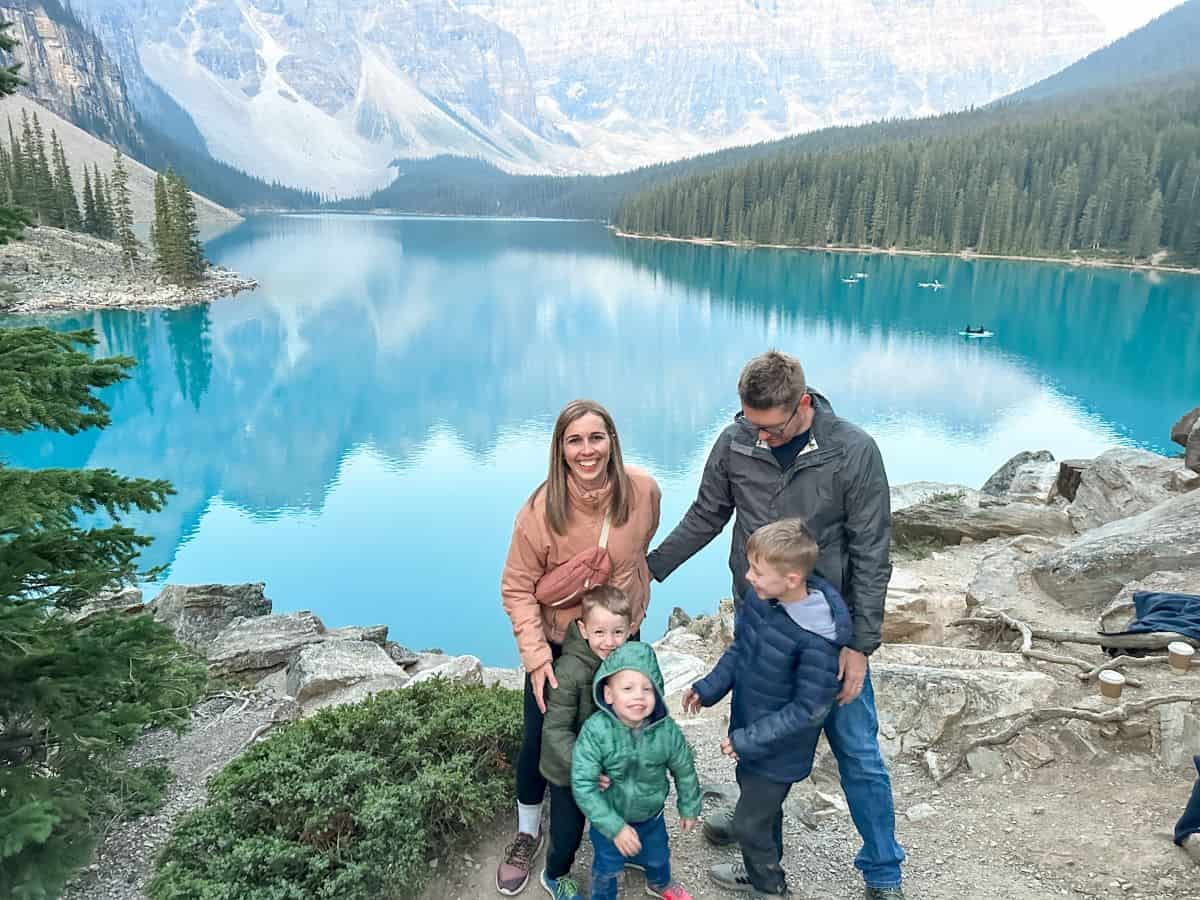 Family of 5 laughing while trying to get the kids to pose for a photo in front of Moraine Lake in Canada