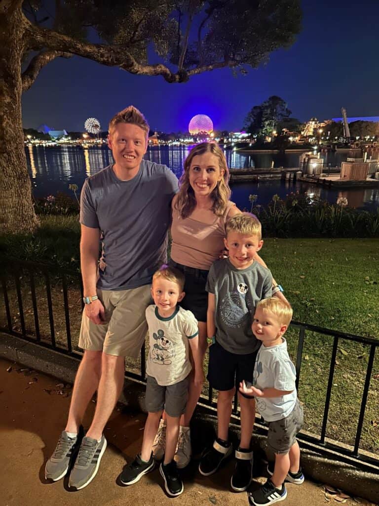 Family of 5 (Dad, Mom, and 3 boys) smiling with Spaceship Earth and fireworks in the background at Epcot